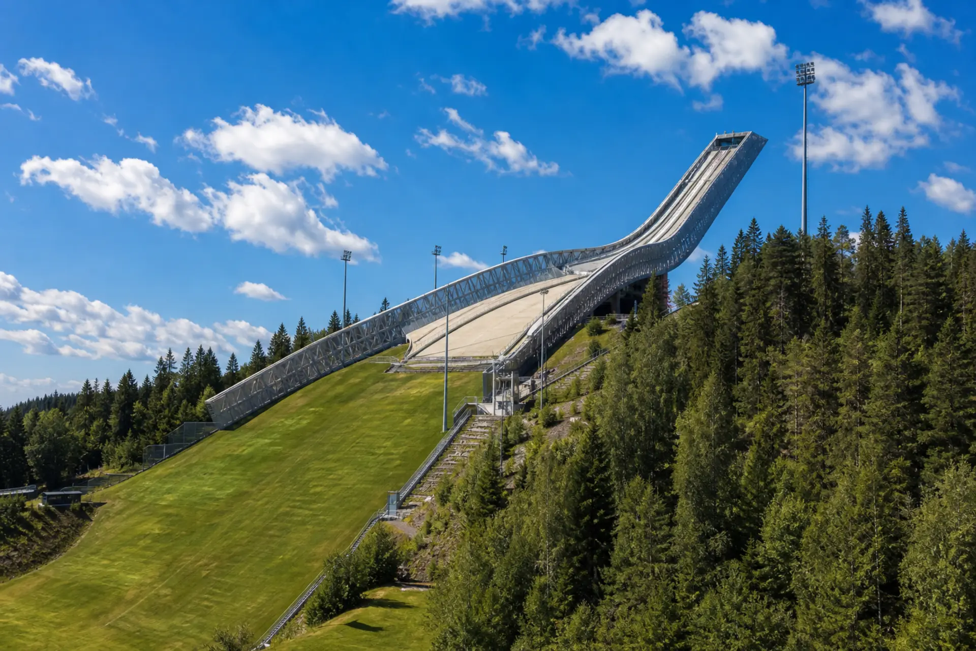 Bílá ocelová věž skokanského můstku Holmenkollen nad lesy a fjordem v Oslu